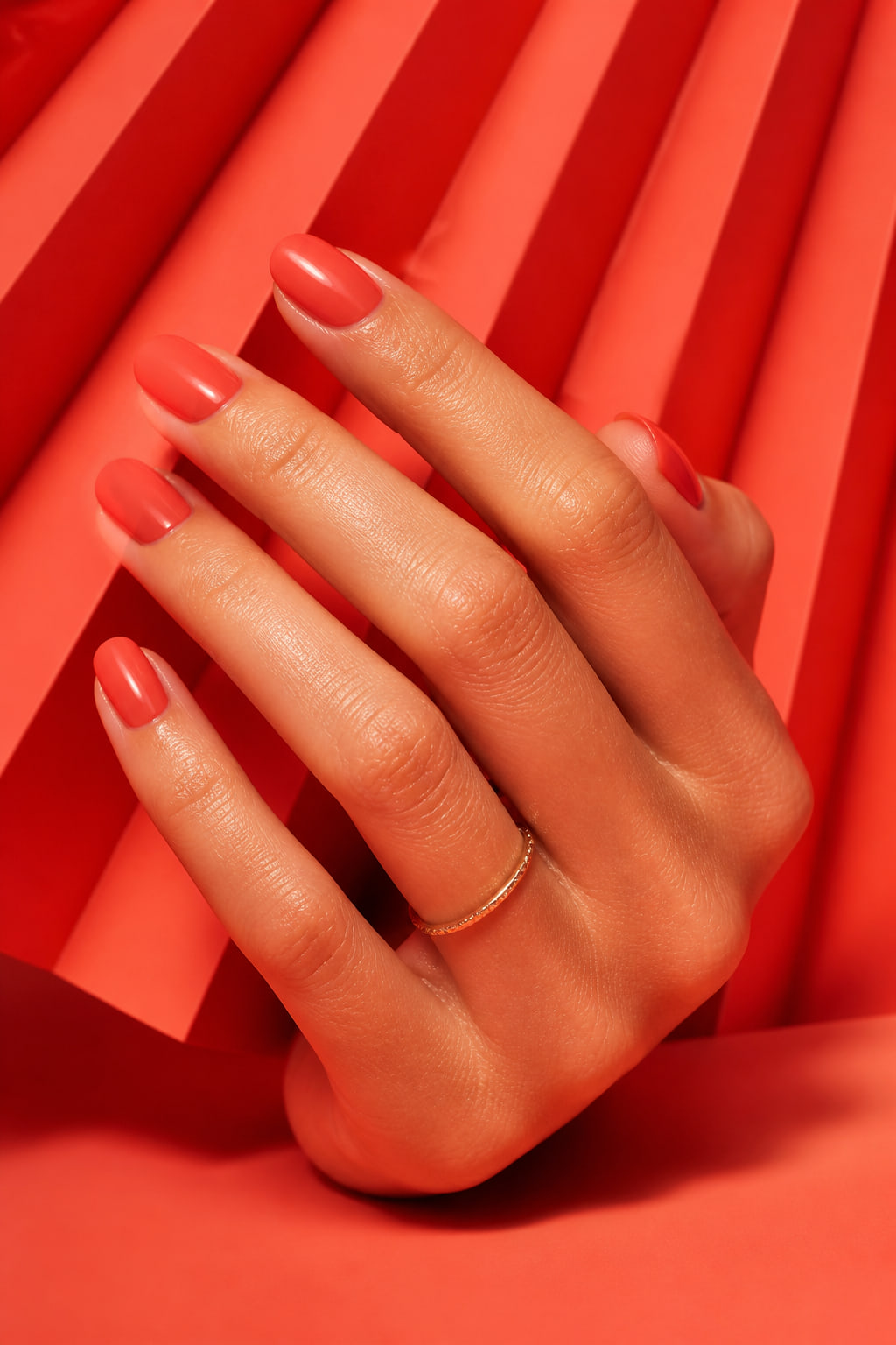 Glossy coral manicure against folded coral paper